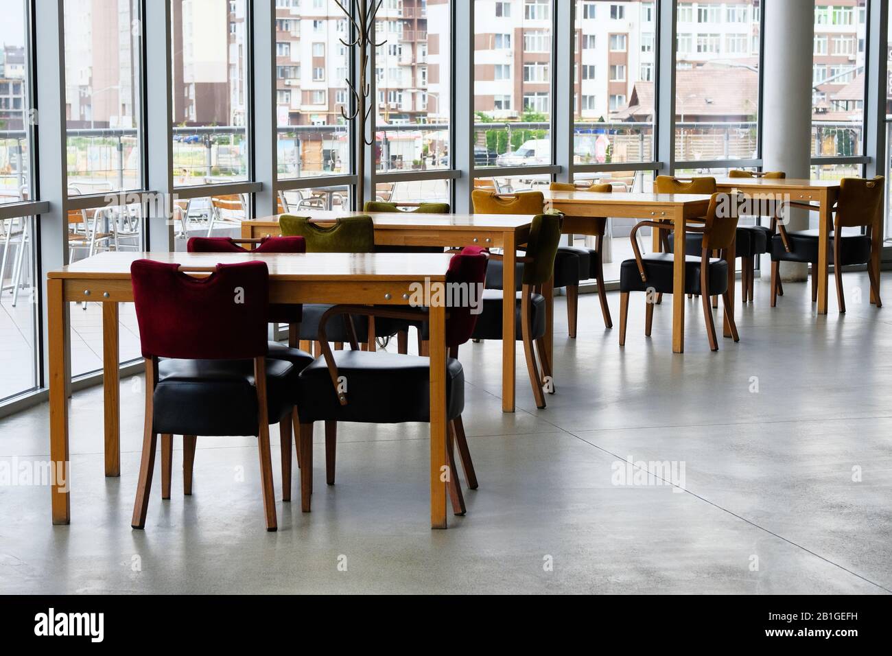 Empty wooden tables and leather chairs stand near the panoramic windows. Food court. Stock Photo