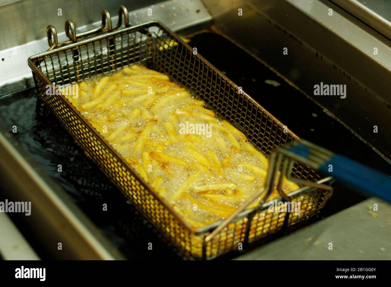 crispy french fries in a deep fat fryer with steel net basket Stock