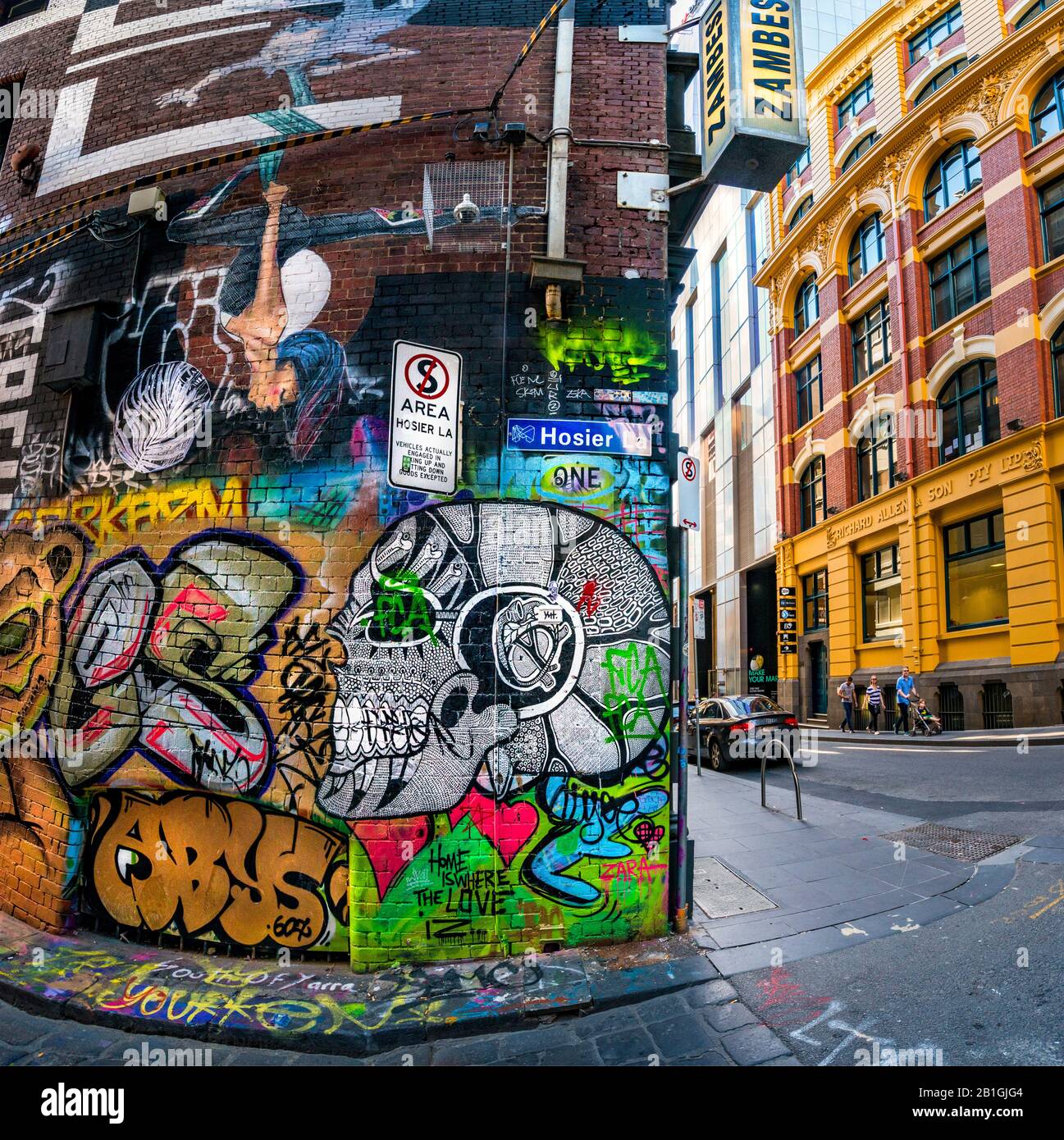 Skull painting and various painted designs, graffiti covered laneway with family strolling down the street in background. Hosier Street, Melbourne Lan Stock Photo