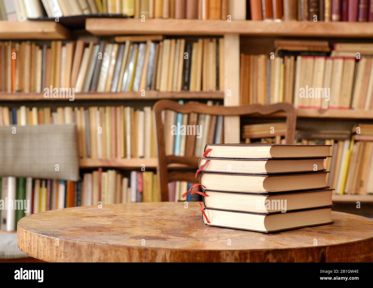 Pile of books on a table and bookshelf in the background Stock Photo