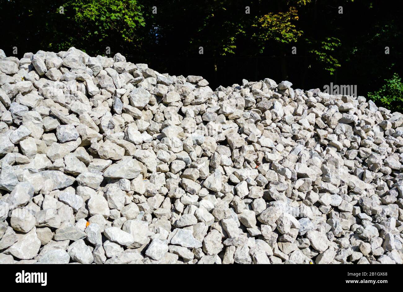Pile of gray rocks and gravel illuminated near trees in shadow Stock ...