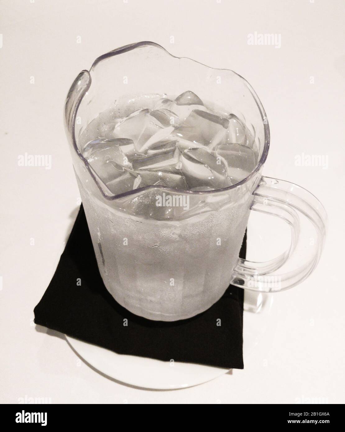 Pitcher with cold water and ice cubes on table napkin. Stock Photo