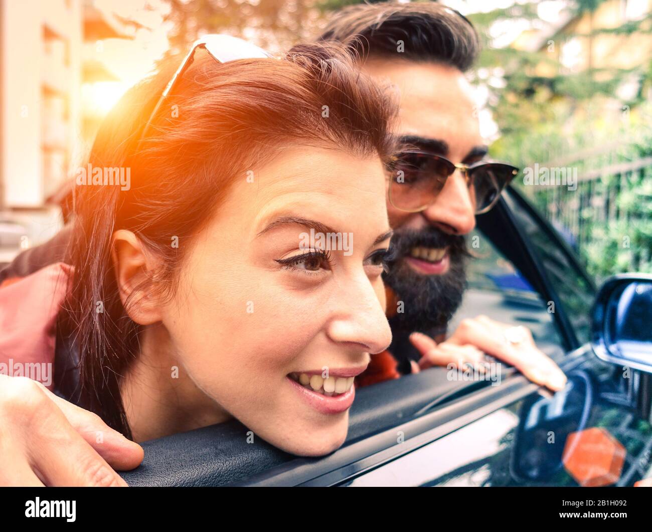 Hipster couple looking outside from their cabrio having fun together - Love and travel concept - Warm light filtered look with sunshine halo Stock Photo