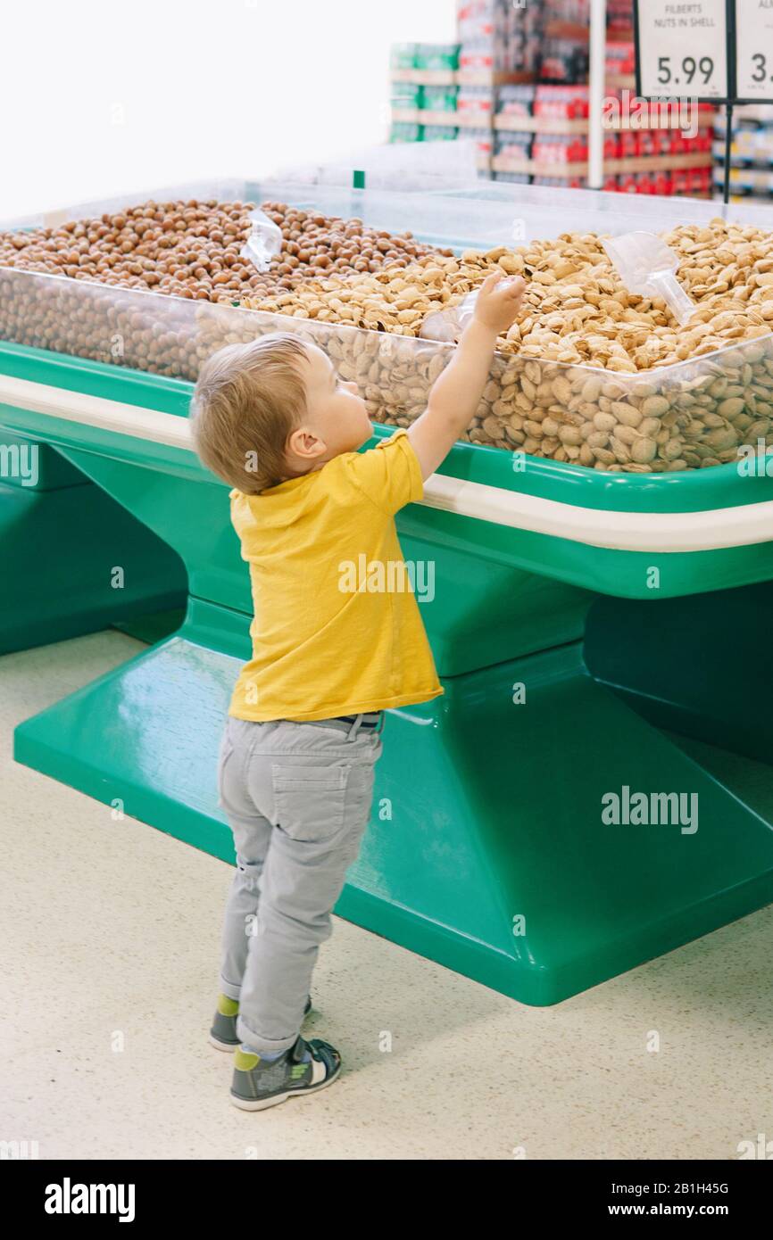 Cute Caucasian baby child choosing nut in supermarket. Funny toddler