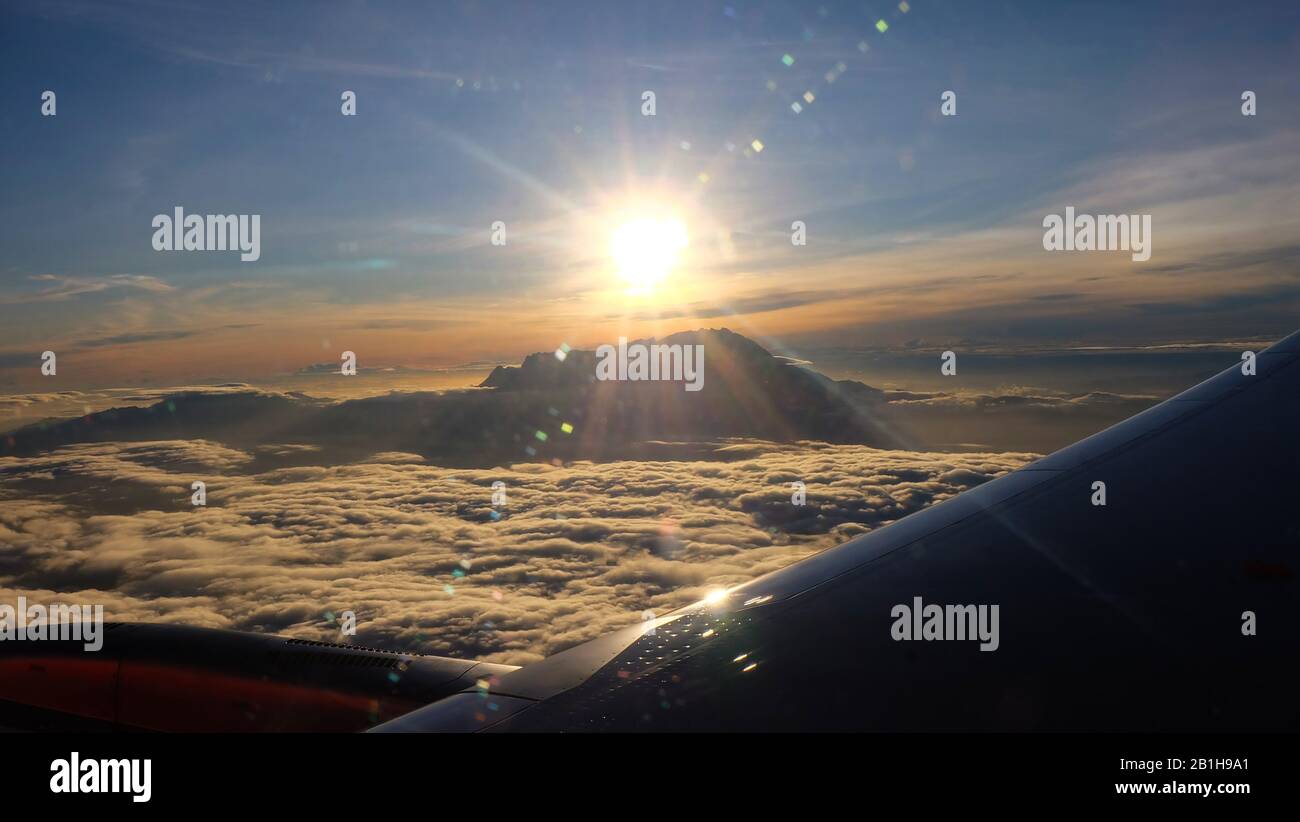 View of the peak of Mount Kinabalu, Sabah, Malaysia, surrounded by sea of clouds, with the rising sun right above its peak. Taken from window of a pla Stock Photo