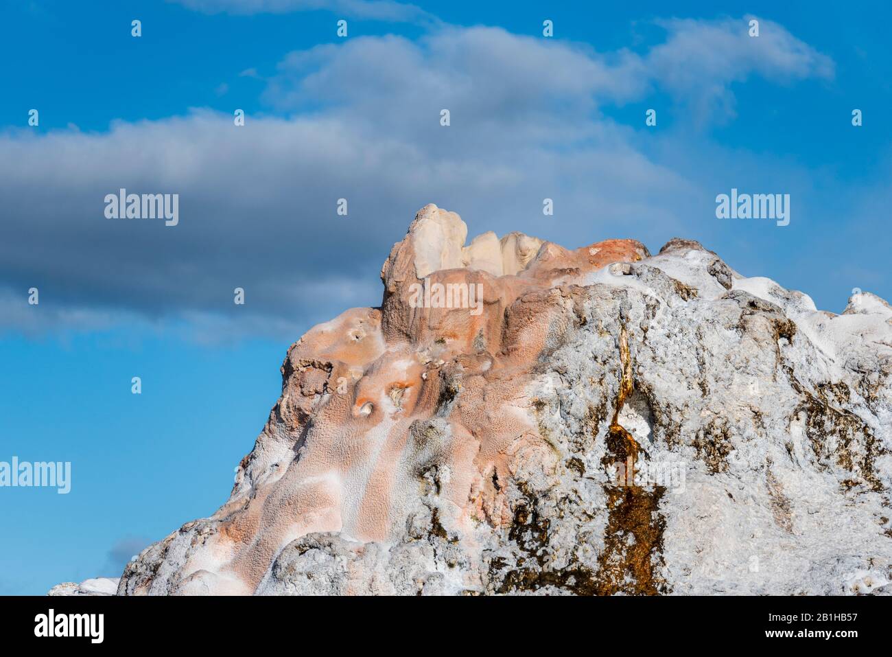Closeup of the top of a geyser against a blue sky with white clouds. Stock Photo