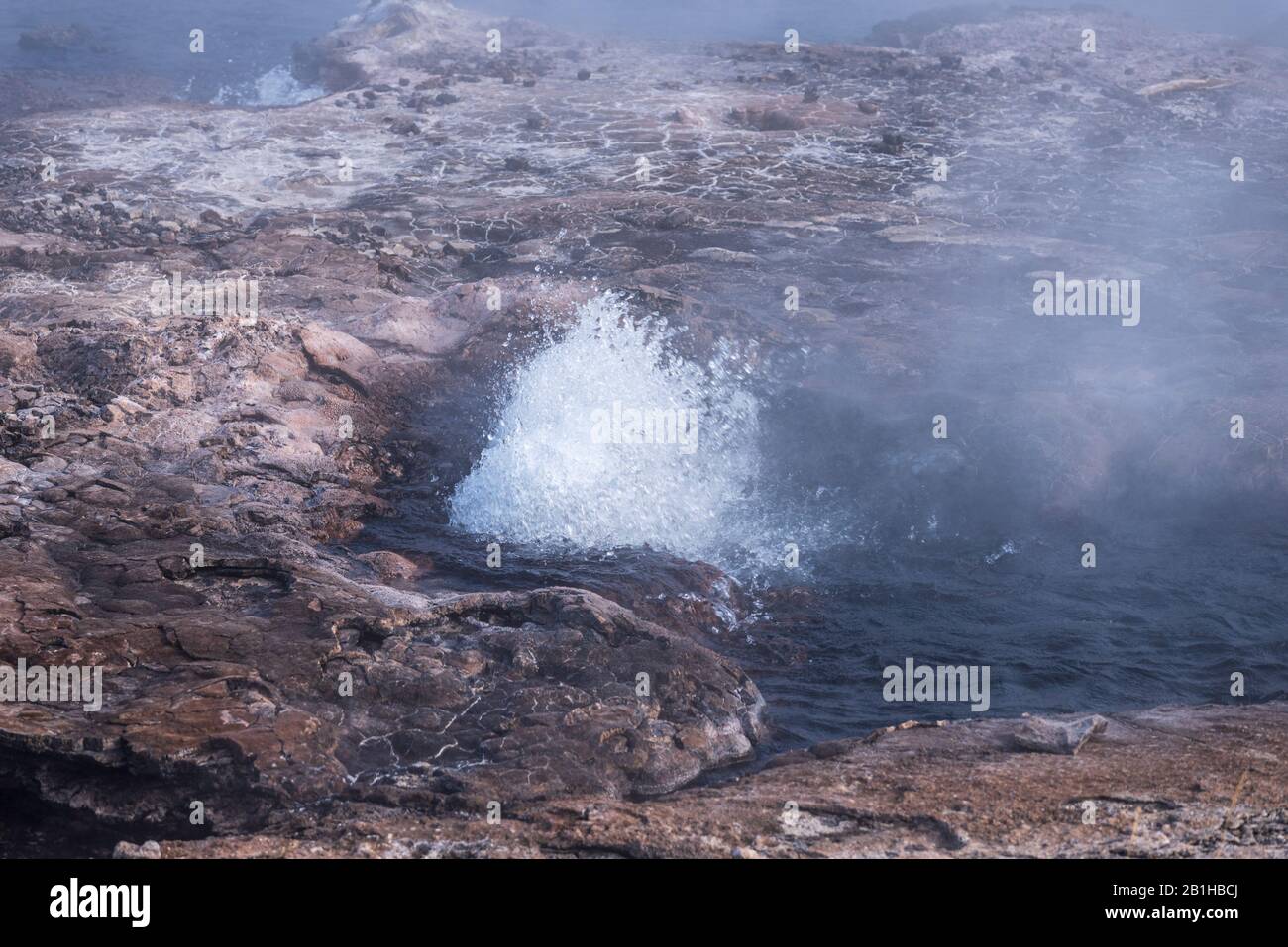Hot spring with boiling hot bubbling water and steam rising up off the