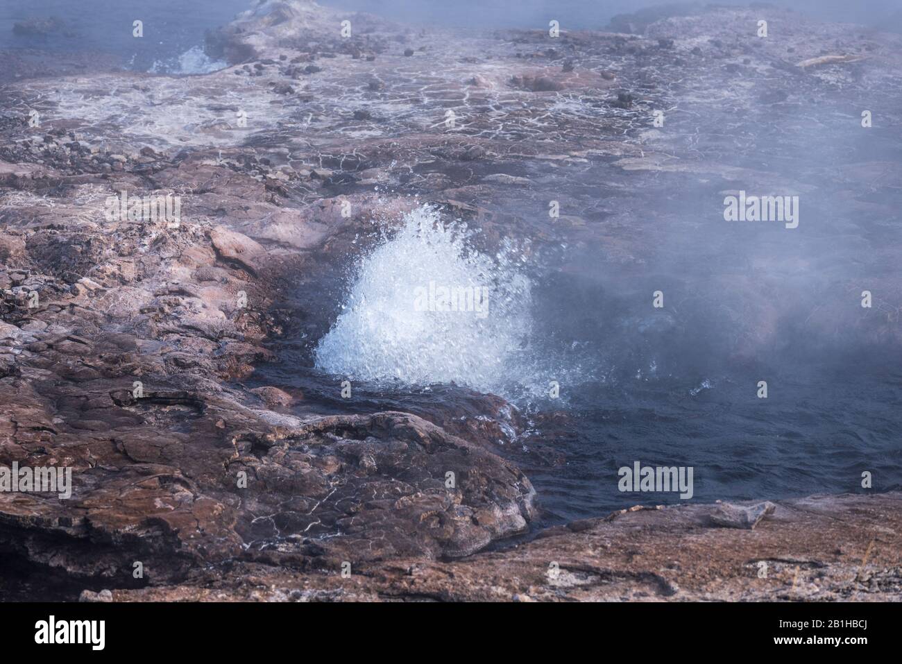 Hot spring with boiling hot bubbling water and steam rising up off the water. brown textured soil around spring. Stock Photo