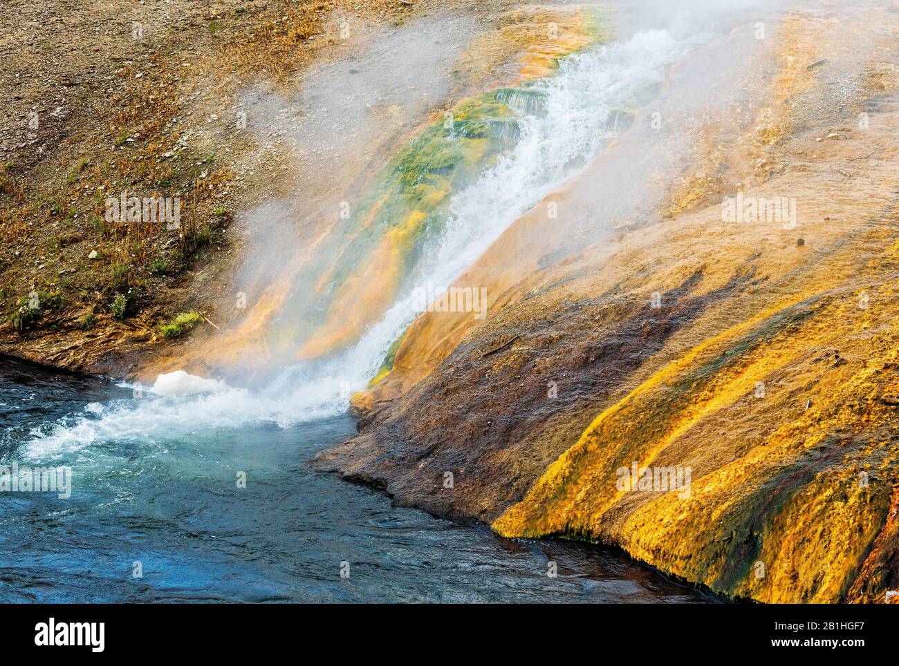 Boiling, steamy hot water running down yellow hillside into cool river