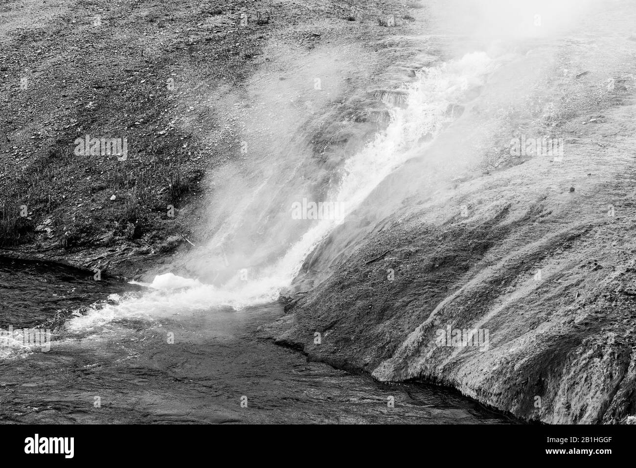 A stream of boiling steamy water running down hillside into river. Stock Photo