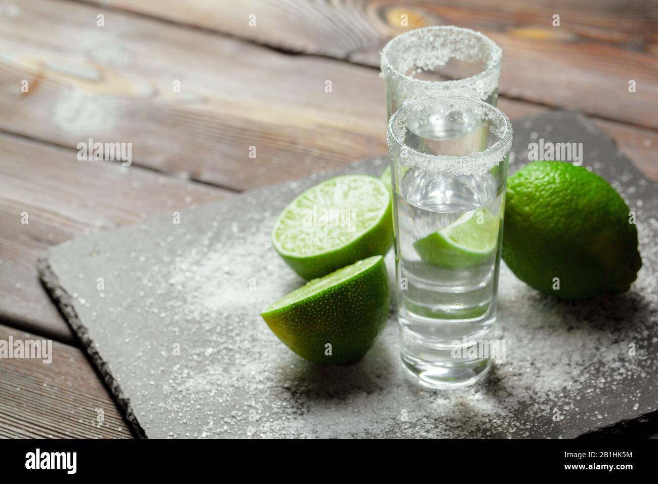 Tequila silver shots with lime slices and salt on wooden board Stock Photo