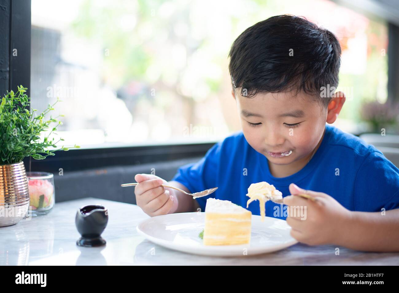 Cute little Asian boy eating cake in bakery shop or cafe Stock Photo