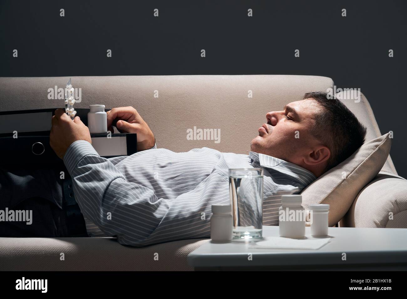 Overworked businessman is lying on the sofa and resting. Pills and