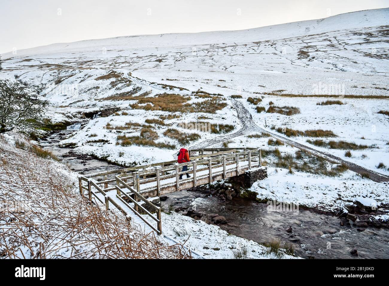A walker crosses a bridge over a stream on the footpath towards Pen y Fan mountain on Brecon Beacons National Park, Wales, after temperatures plummeted overnight across Britain, and forecasters warned of more ice and snow over the next 24 hours. Stock Photo