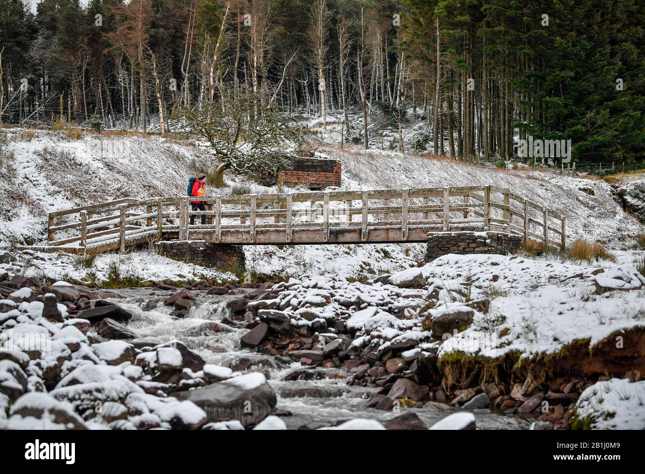 A walker crosses a bridge over a stream on the footpath towards Pen y Fan mountain on Brecon Beacons National Park, Wales, after temperatures plummeted overnight across Britain, and forecasters warned of more ice and snow over the next 24 hours. Stock Photo