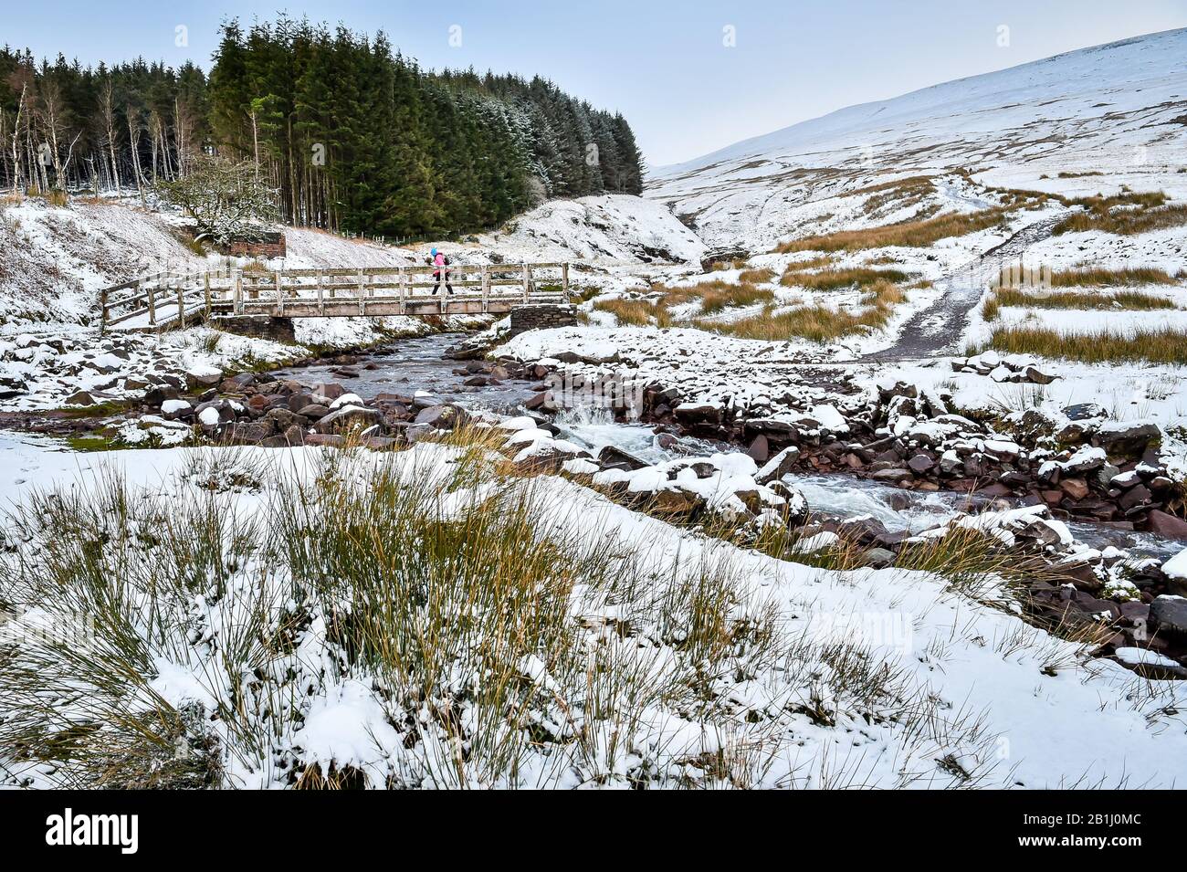 A walker crosses a bridge over a stream on the footpath near Pen y Fan mountain on Brecon Beacons National Park, Wales, after temperatures plummeted overnight across Britain, and forecasters warned of more ice and snow over the next 24 hours. Stock Photo