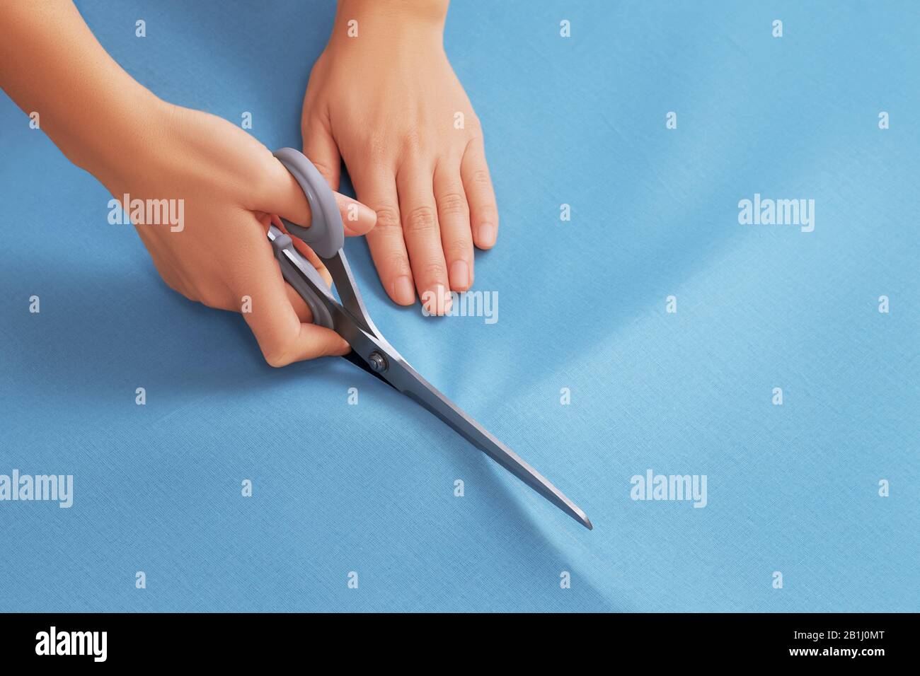 Top view on the hands of a professional tailor woman who cuts blue ...