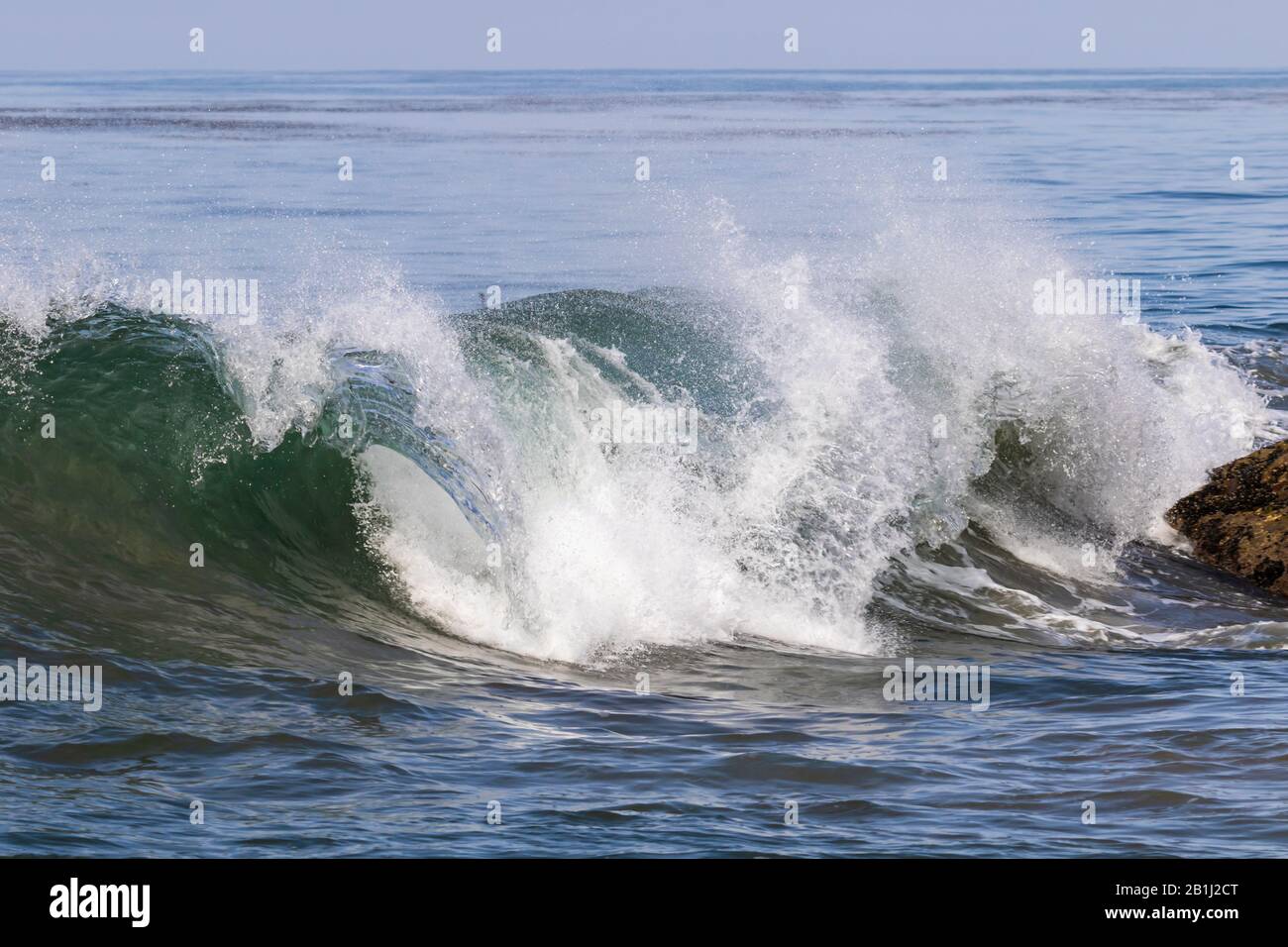 Curling wave at Leo Carrillo State Beach, Malibu, California. Rock nearby; pacific ocean in distance. Stock Photo