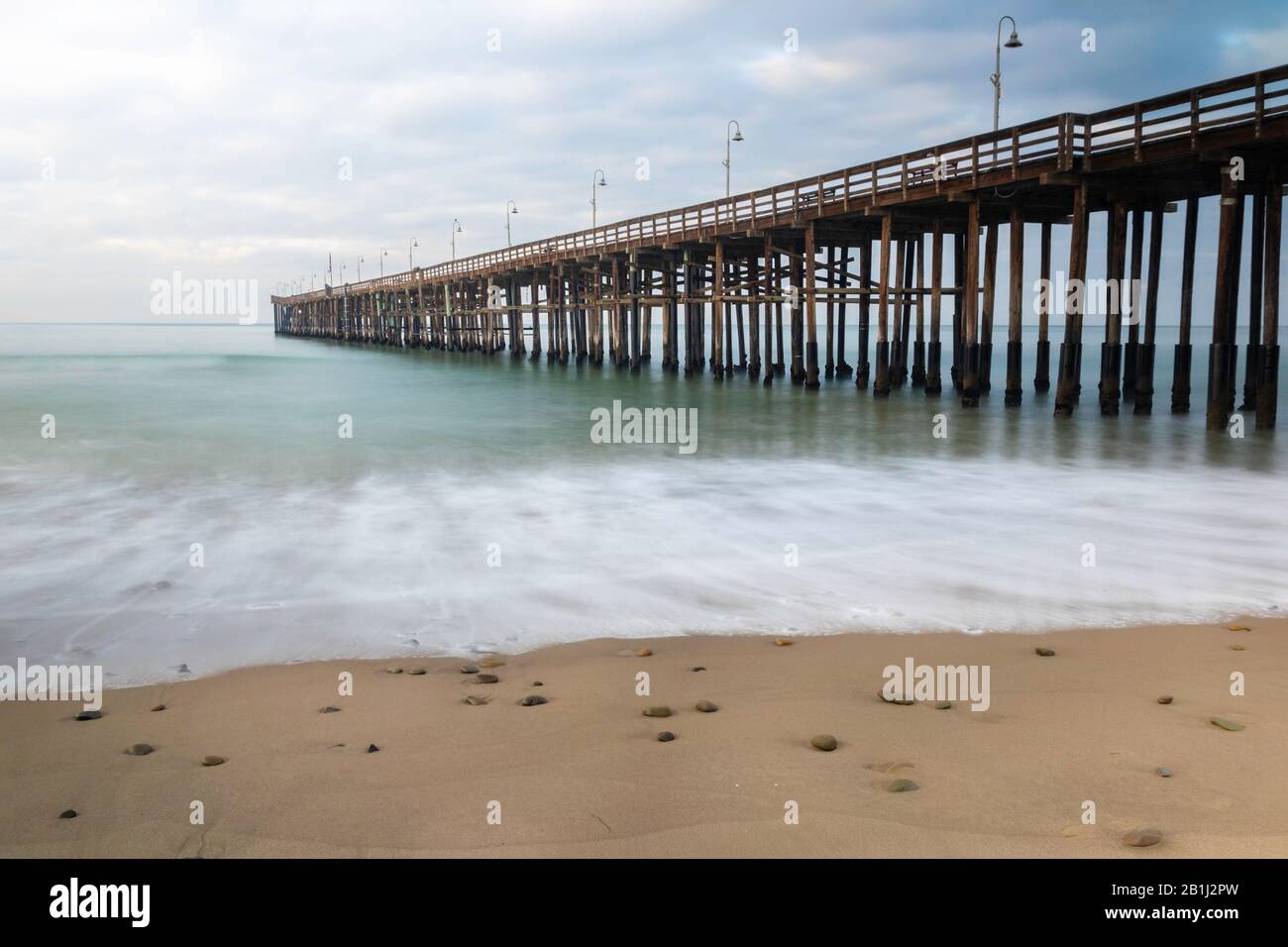 Pier at Ventura, California; view from beach, extending into the water. Green ocean, cloudy sky. Stock Photo