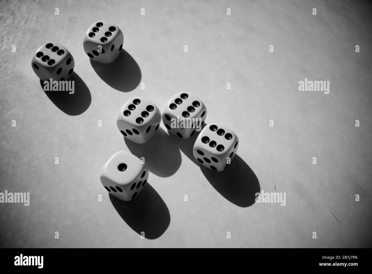 The miserable realisation of gambling addiction. A gloomy composition of dices on a scratched surface. Black and white photo. Vignetted. Stock Photo