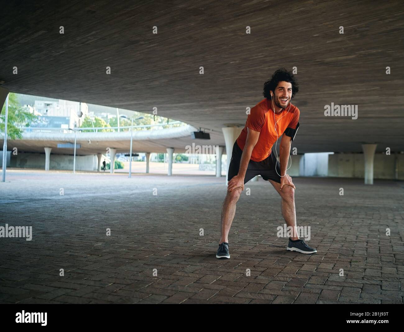 Portrait of young attractive tired man exhausted after outdoors running workout on city street under the concrete bridge - new year new you Stock Photo