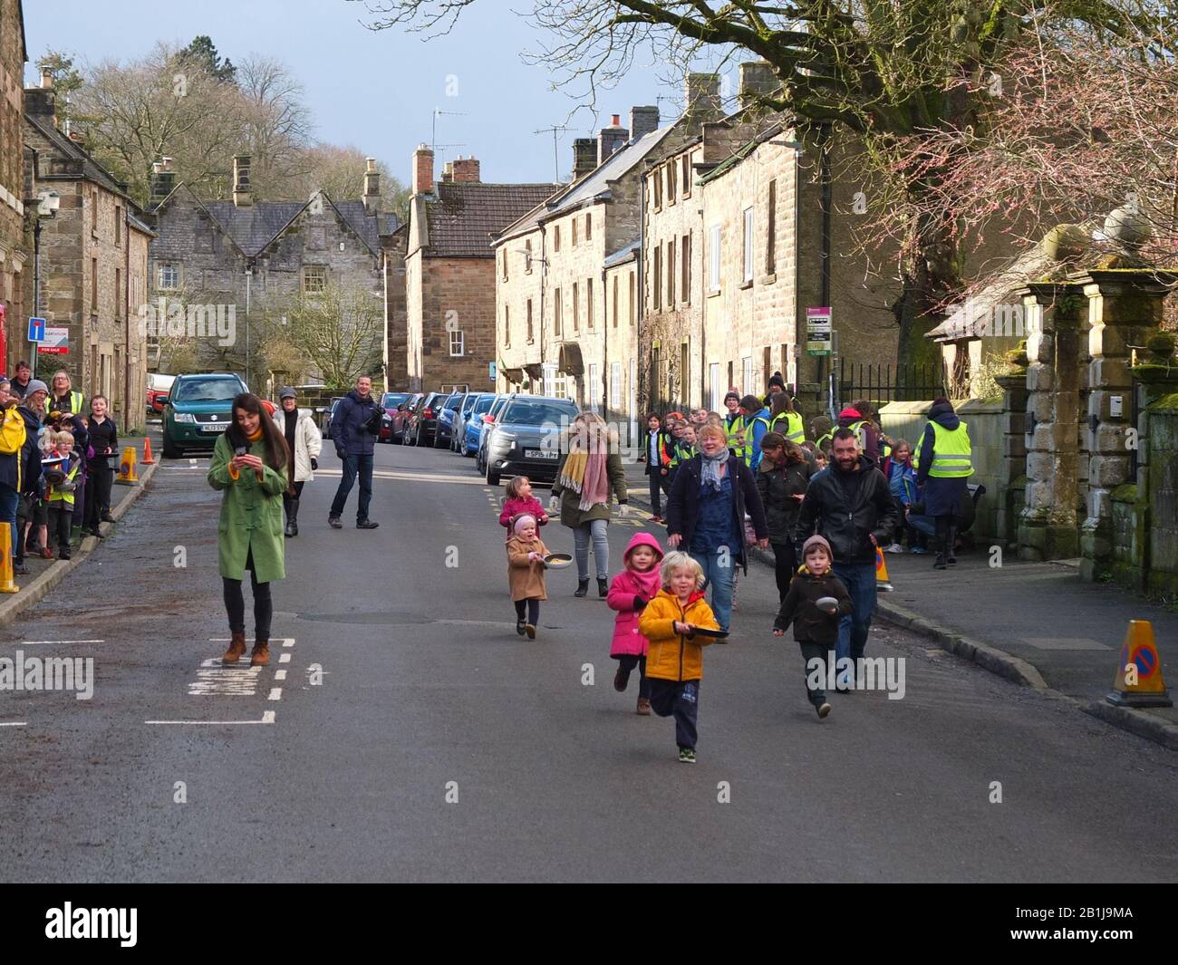Toddlers race down village main street with frying pans and pancakes during Winster Pancake Races Shrove Tuesday Pancake Day Derbyshire UK Stock Photo