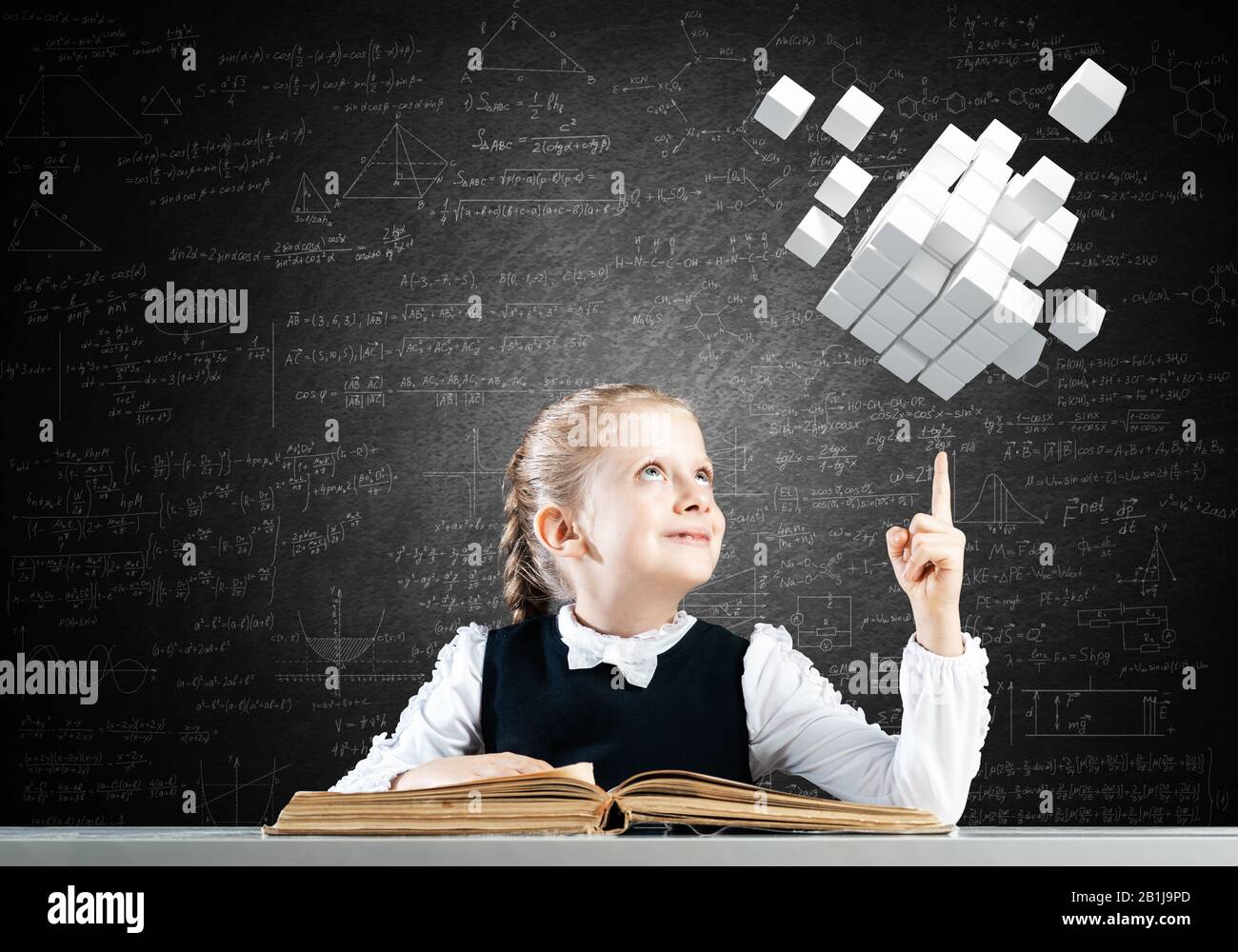 Smiling little girl sitting at desk with open book Stock Photo - Alamy