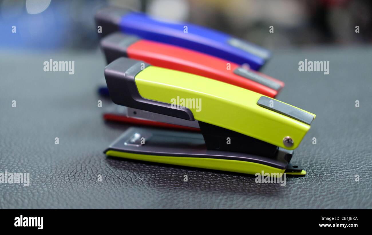 Three staplers of green, red and blue standing next to each other on a black leather surface Stock Photo