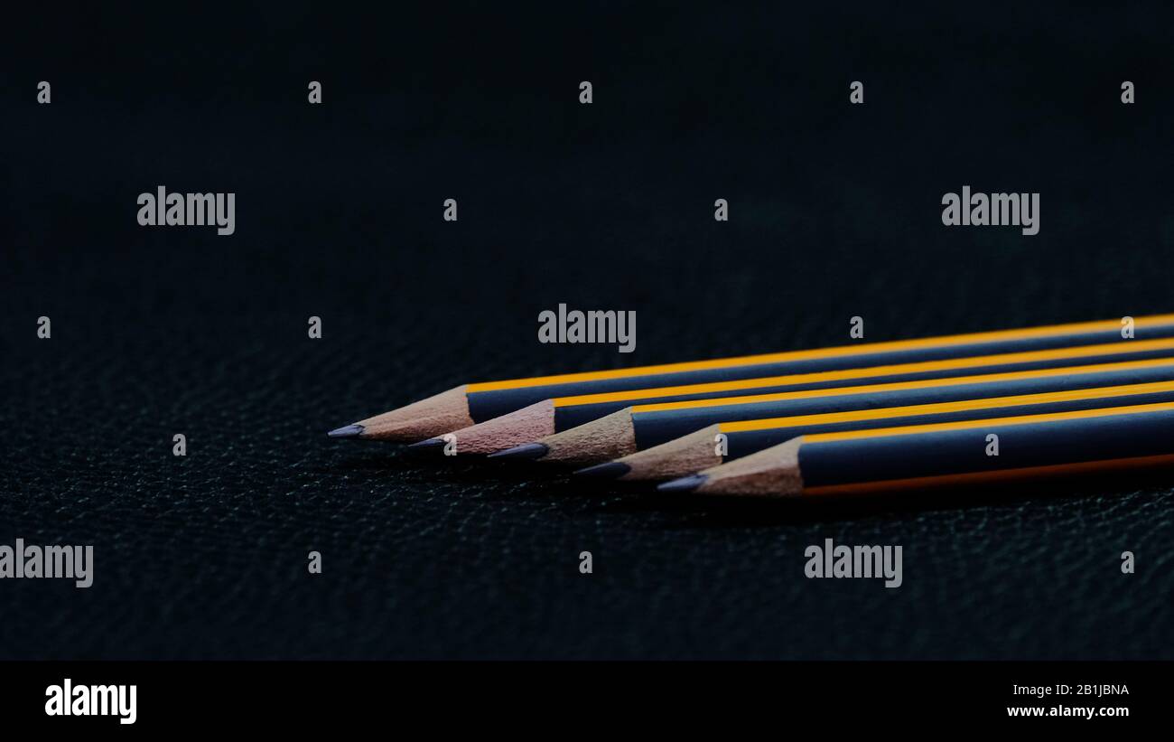 Five black pencils with an orange stripe lying in a row one after another diagonally on a black background Stock Photo