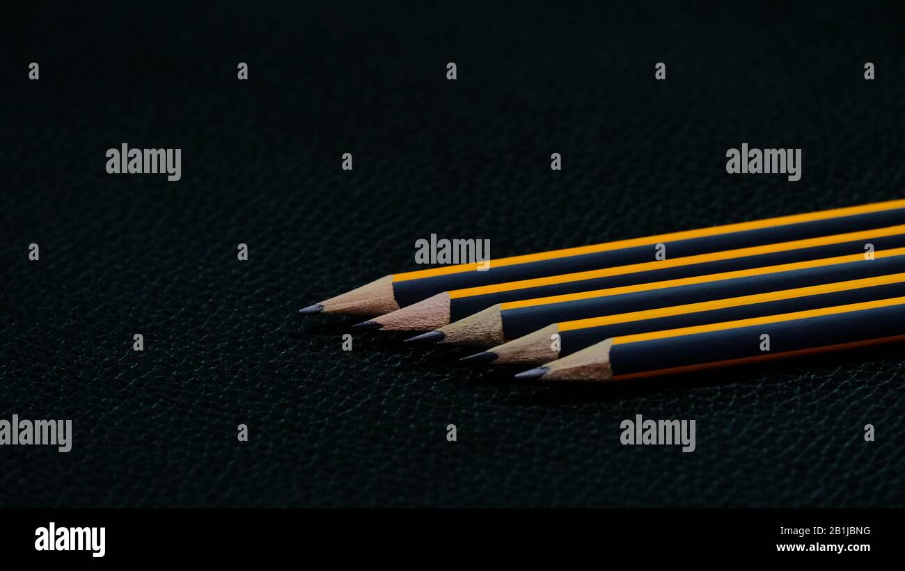 Five black pencils with an orange stripe lying in a row one after another diagonally on a black background from a different angle Stock Photo