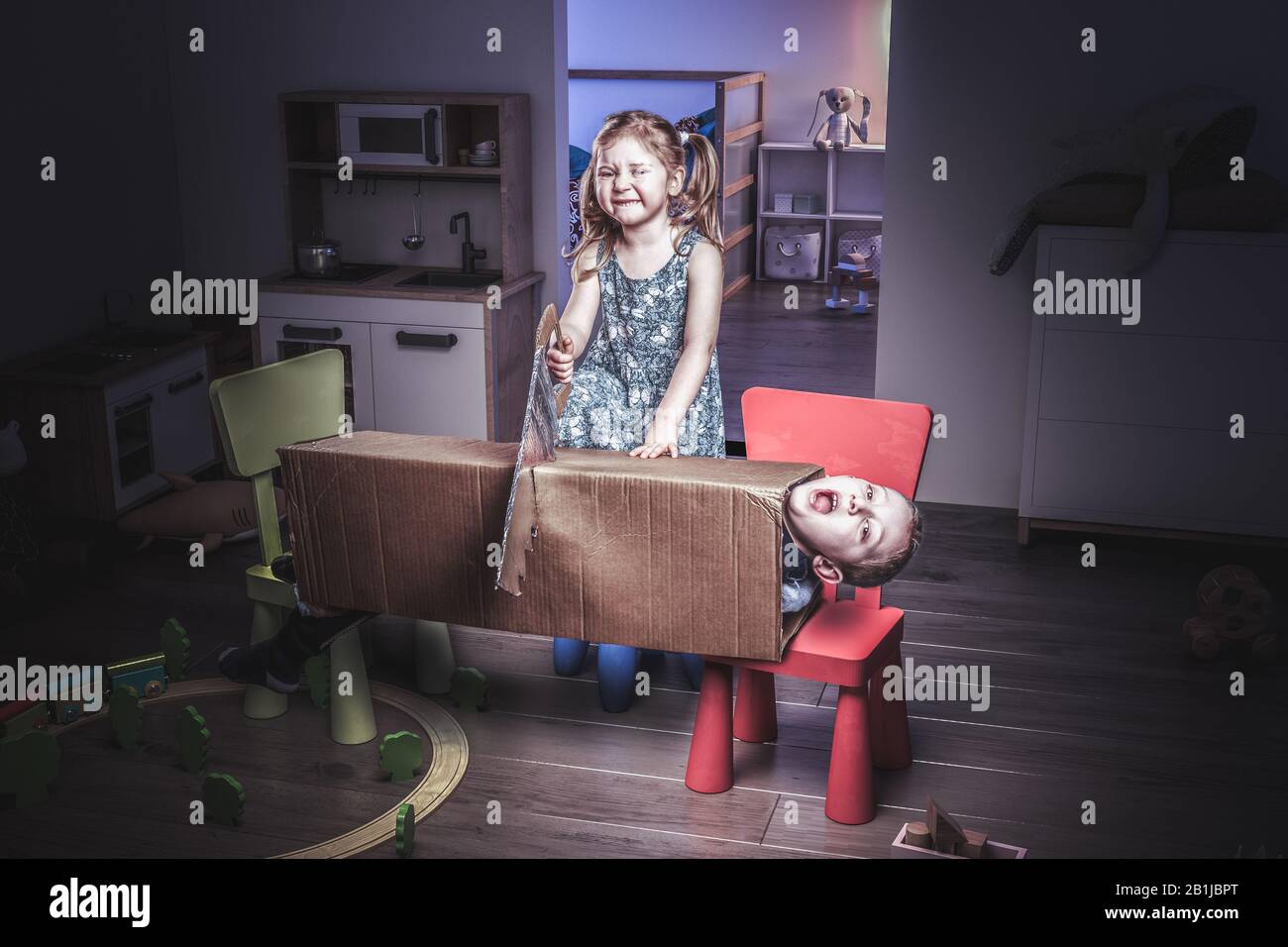 little 3 year old girl plays the magician and tries to cut her brother in two with a saw. Funny image, concept of carefree and childhood. Stock Photo