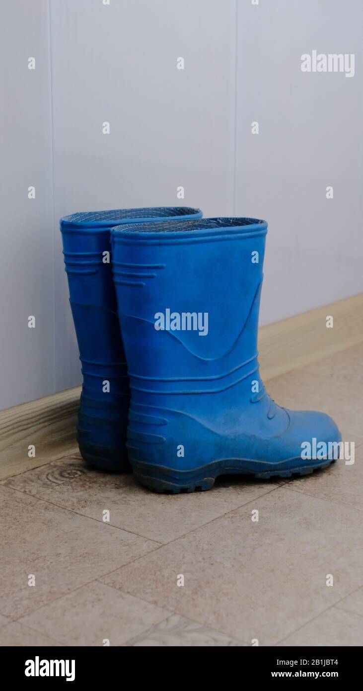 A pair of blue children's rubber boots standing along a white wall on  linoleum Stock Photo - Alamy