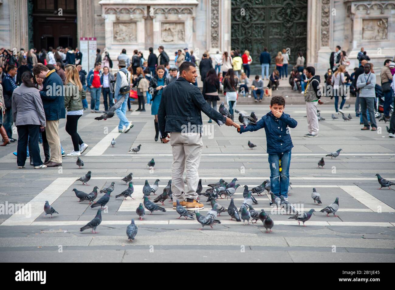 Boy with father playing with pigeons on crowded Piazza del Duomo Stock Photo