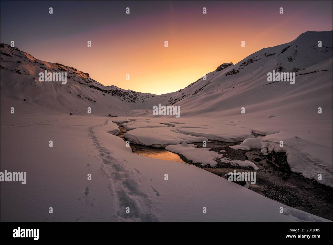 Footprints in the snowscape of the Engstligenalp along the Engstligen brook at dusk Stock Photo