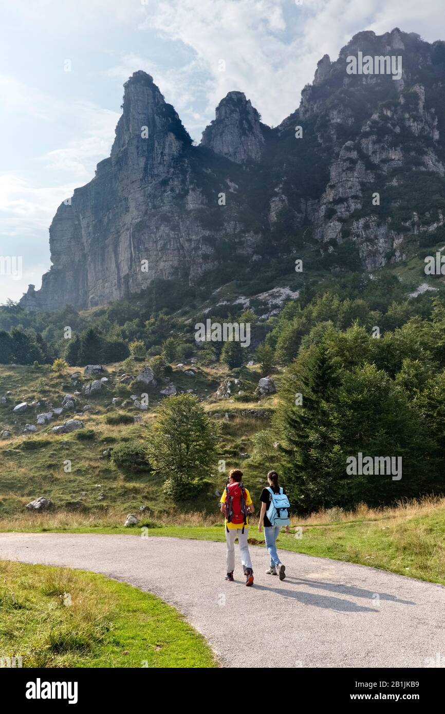 Two hikers walk in Campogrosso pass. In the background Mount La Sisilla. Piccole Dolomiti, Vicenza province, Veneto, Italy, Europe. Stock Photo