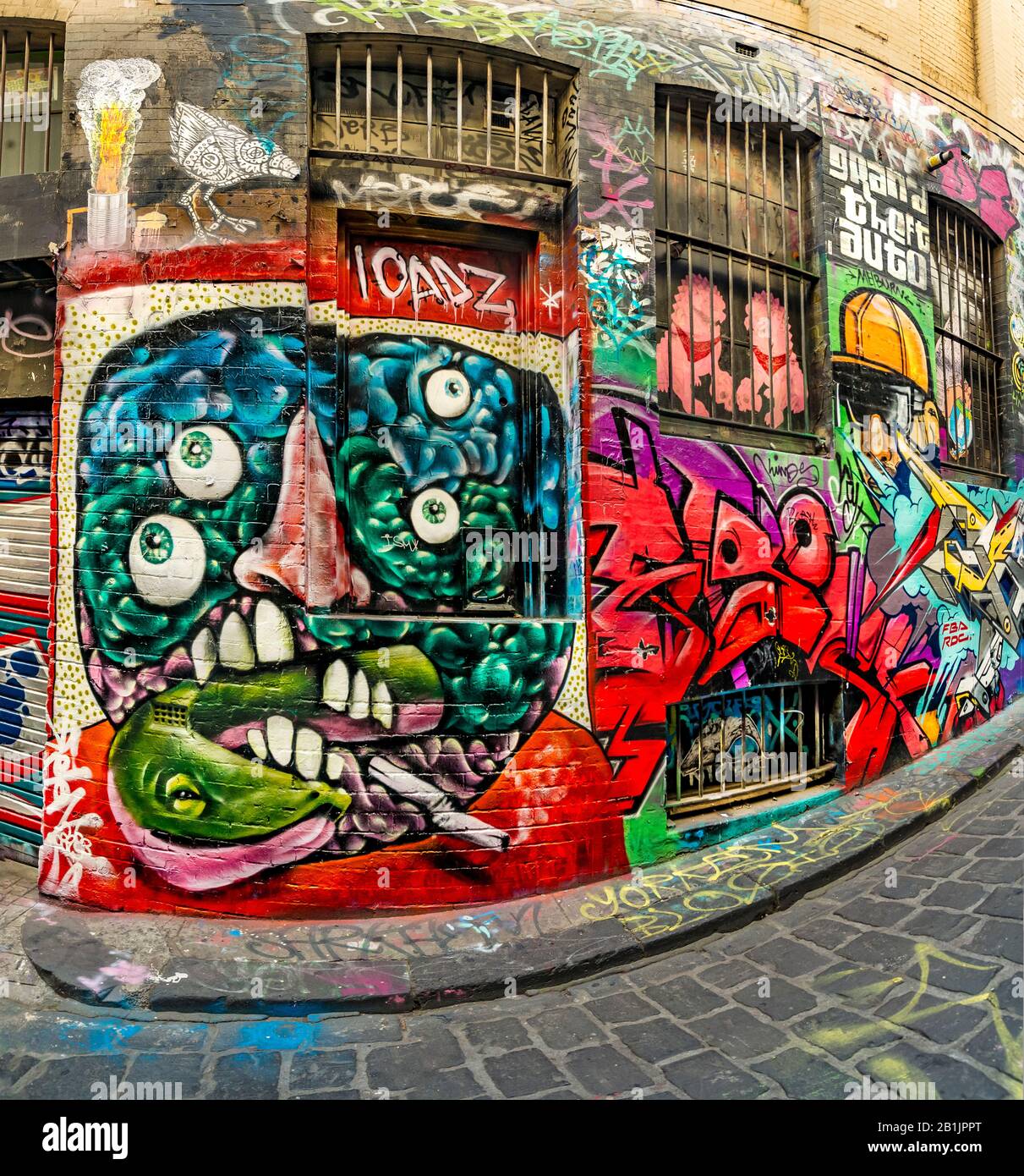 Brightly coloured mad humerous face with many eyes smoking, graffiti filled alley way, Hosier Street, Melbourne Lanes, Melbourne, Victoria, Australia Stock Photo