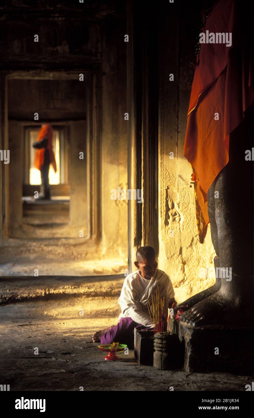 Angkor Wat Interior. Woman placing offerings to the gods. Large statues of Vishnu clothed in orange fabric. Dawn, Stock Photo