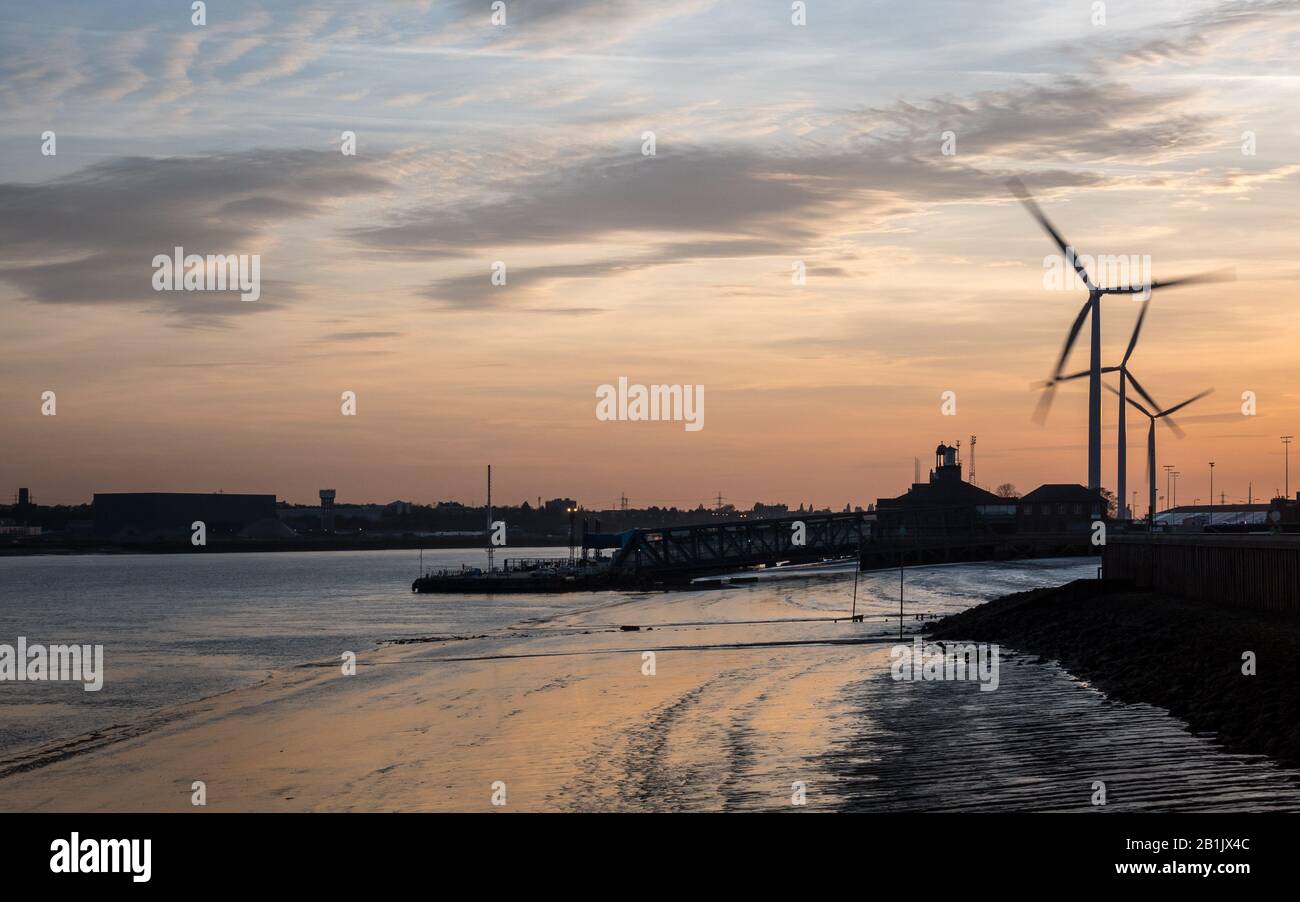 Dusk at the Port of Tilbury, Essex, UK. Sunset view of the low tide of the River Thames and wind turbines turning in the background. Stock Photo