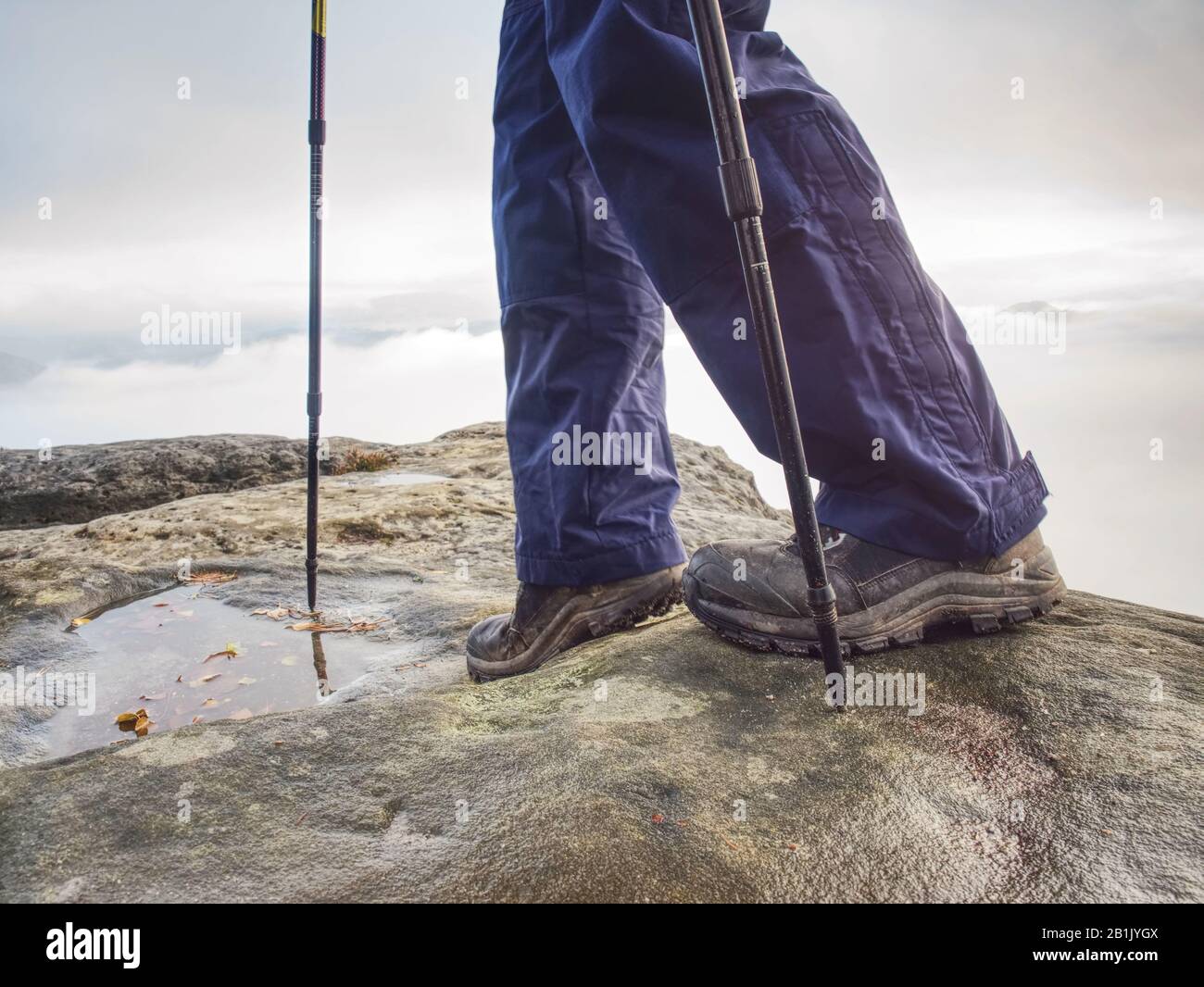 man hiker legs stand on mountain peak rock. Slippery  journey at the edge Stock Photo