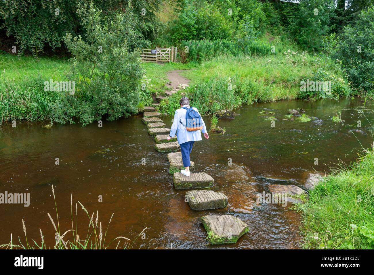 Summer view of a lady crossing stepping stones over a river Stock Photo