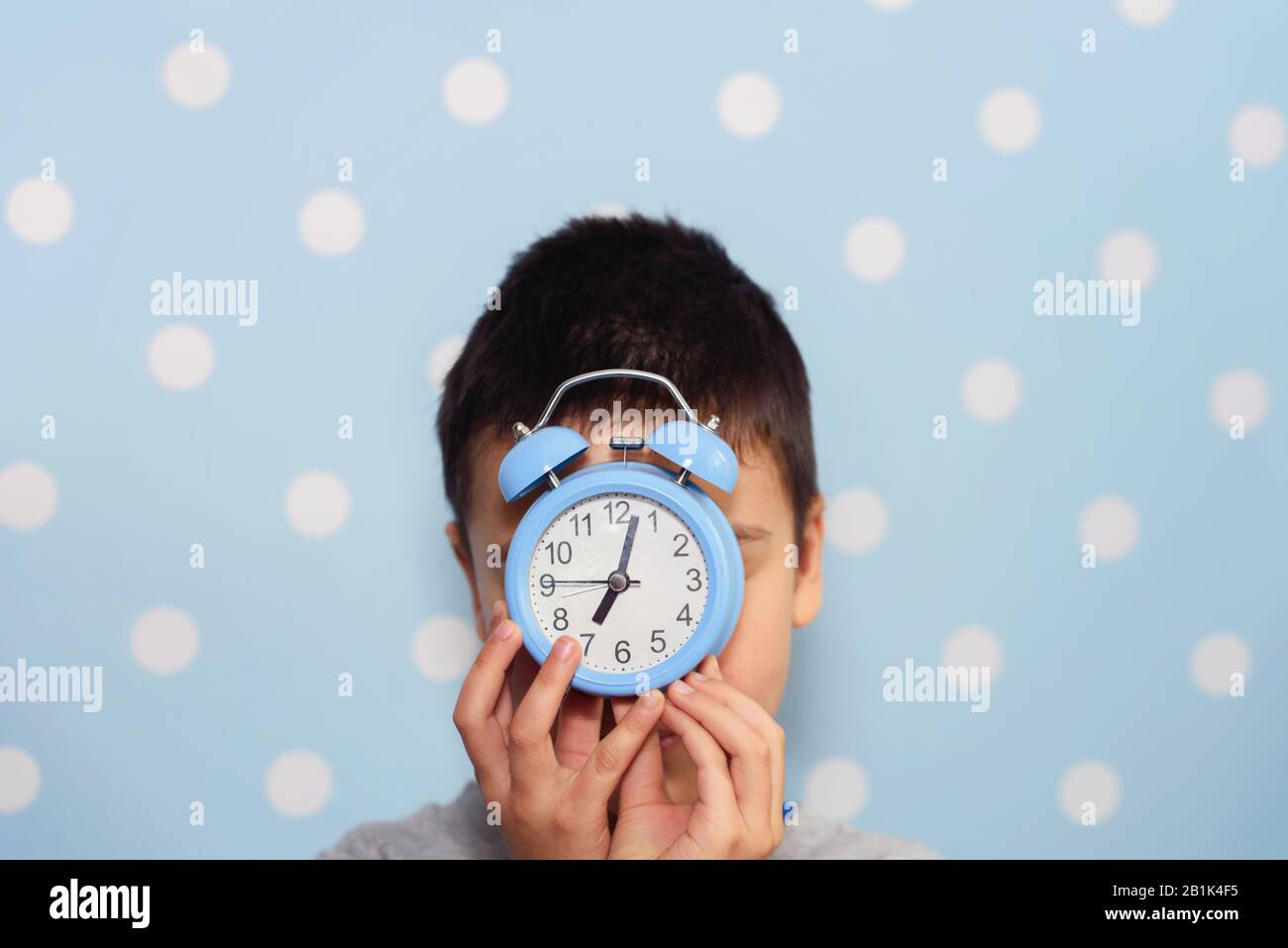 Cute little boy with alarm clock, People, school, time and lifestyle concept. sleepyhead or early bird. Sleeping child with alarm clock in front of fa Stock Photo