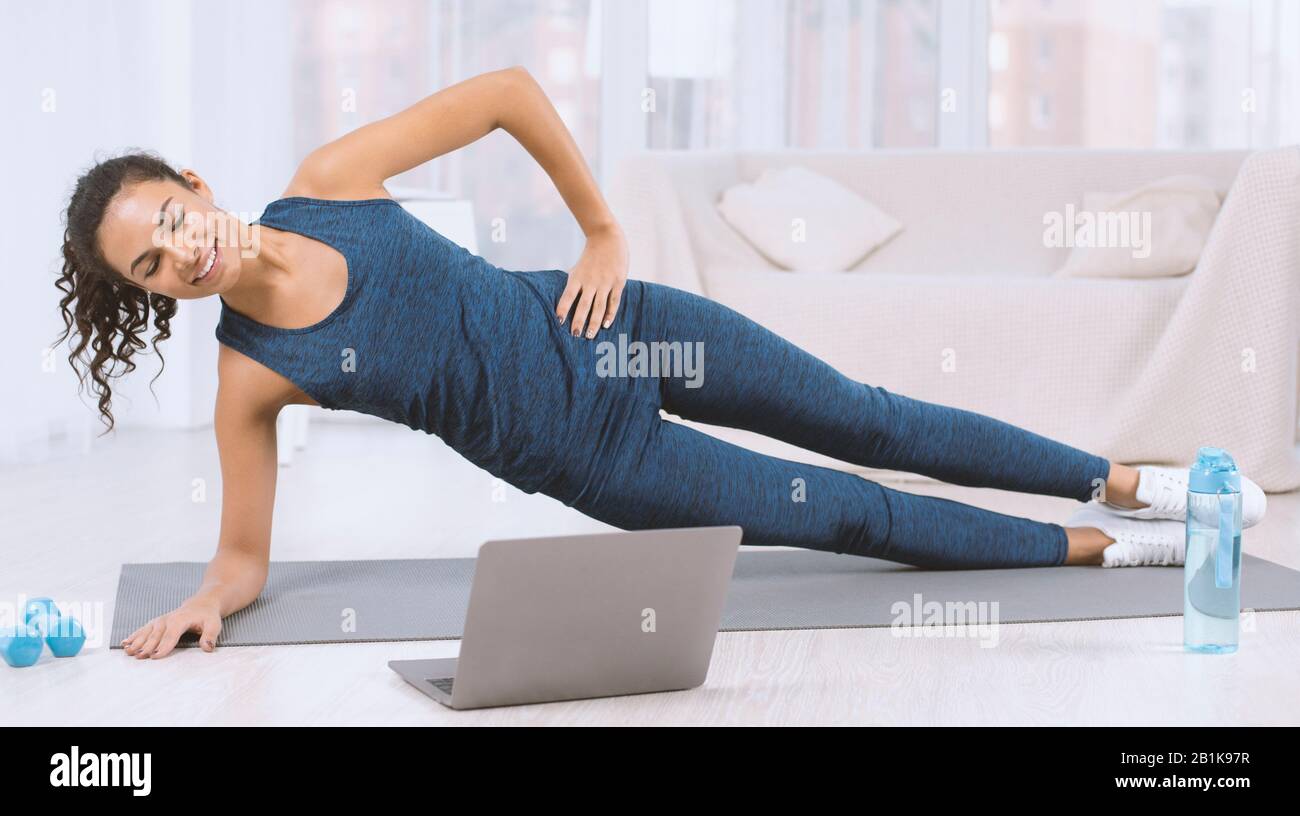 Smiling Latin Woman Doing Side Plank Exercise While Watching Workout smiling-latin-woman-doing-side-plank-exercise-while-watching-workout