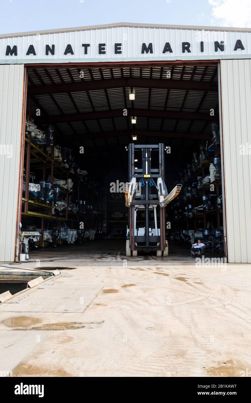 A forklift driver dwarfed by his machine rests between calls for service at the Manatee Marina in Port Salerno, Florida, USA. Stock Photo