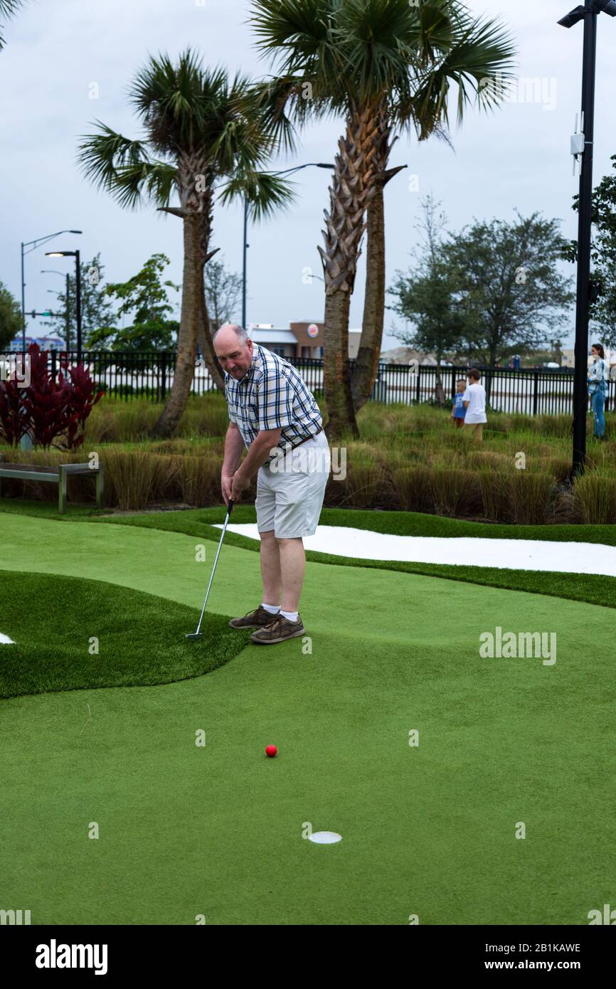 A man wearing a plaid shirt and shorts plays mini golf at the PopStroke Miniature Golf Coarse in