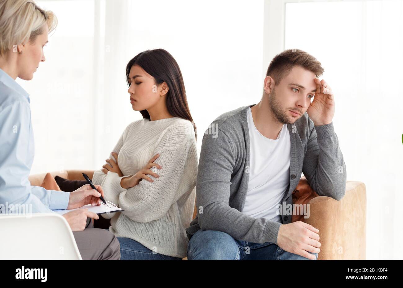 Indifferent Spouses Having Conflict Sitting Back-To-Back In Psychologist's Office Stock Photo