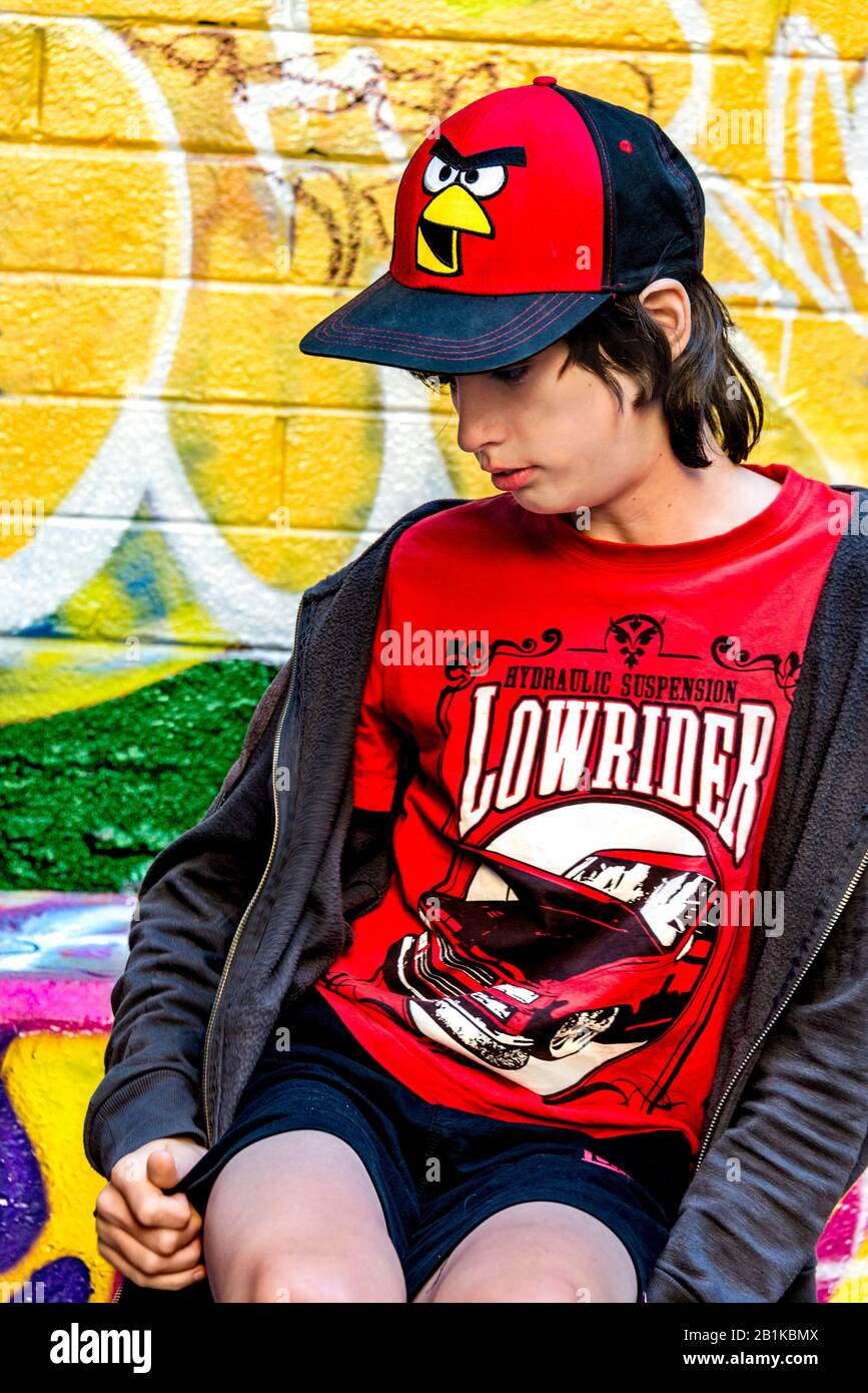 Young boy sitting on a ledge against a brightly coloured graffiti wall, Hosier Street, Melbourne Lanes, Melbourne, Victoria, Australia Stock Photo