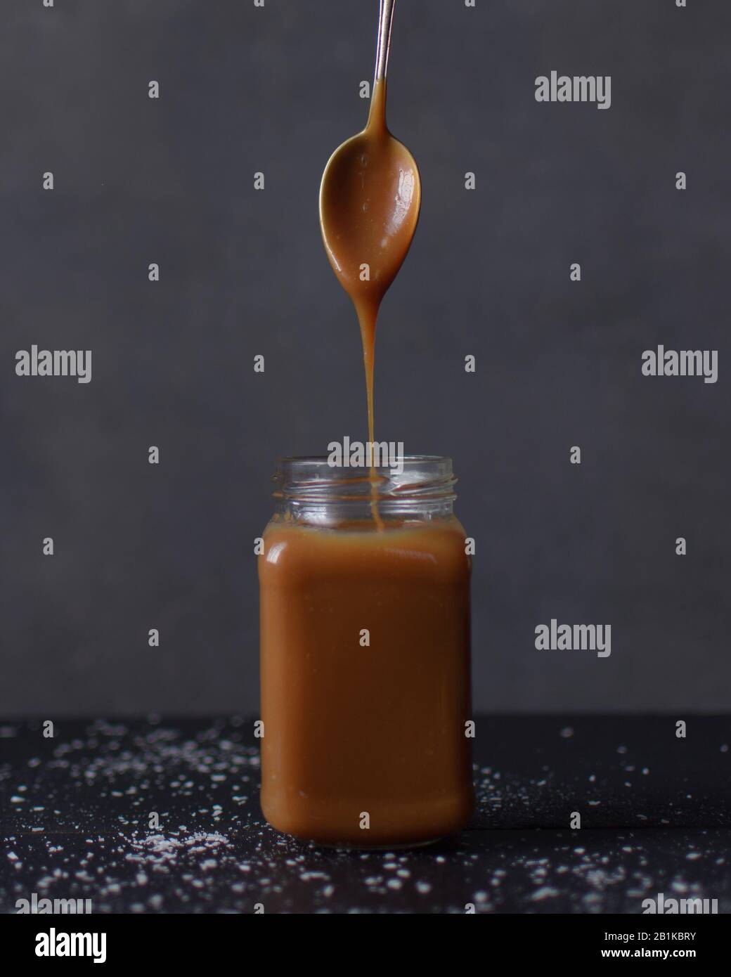 Salted caramel sauce dripping from a spoon into a glass jar, Caramel