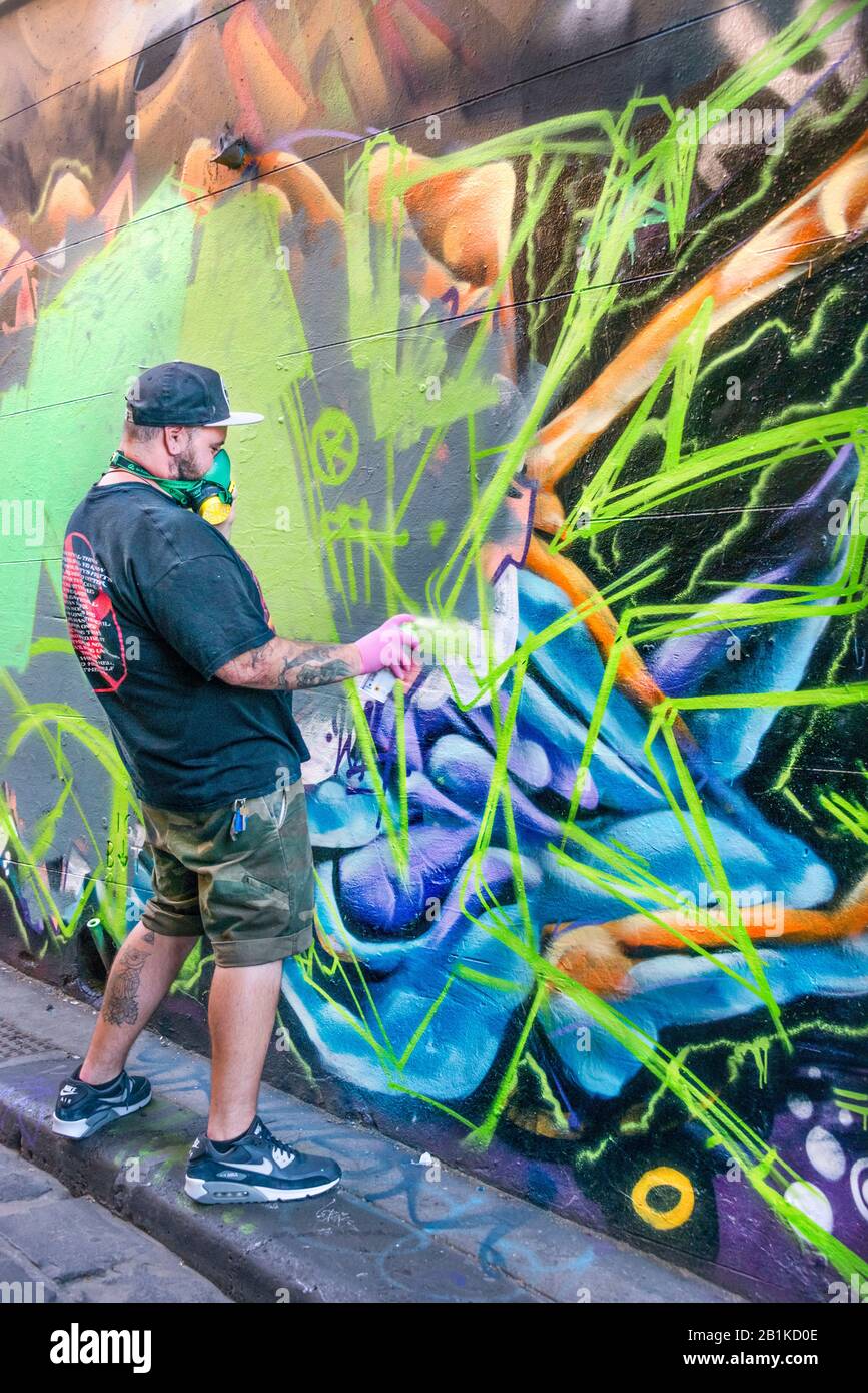 Young man with mask spray painting graffiti in back alley way, Hosier Street, Melbourne Lanes, Melbourne, Victoria, Australia Stock Photo