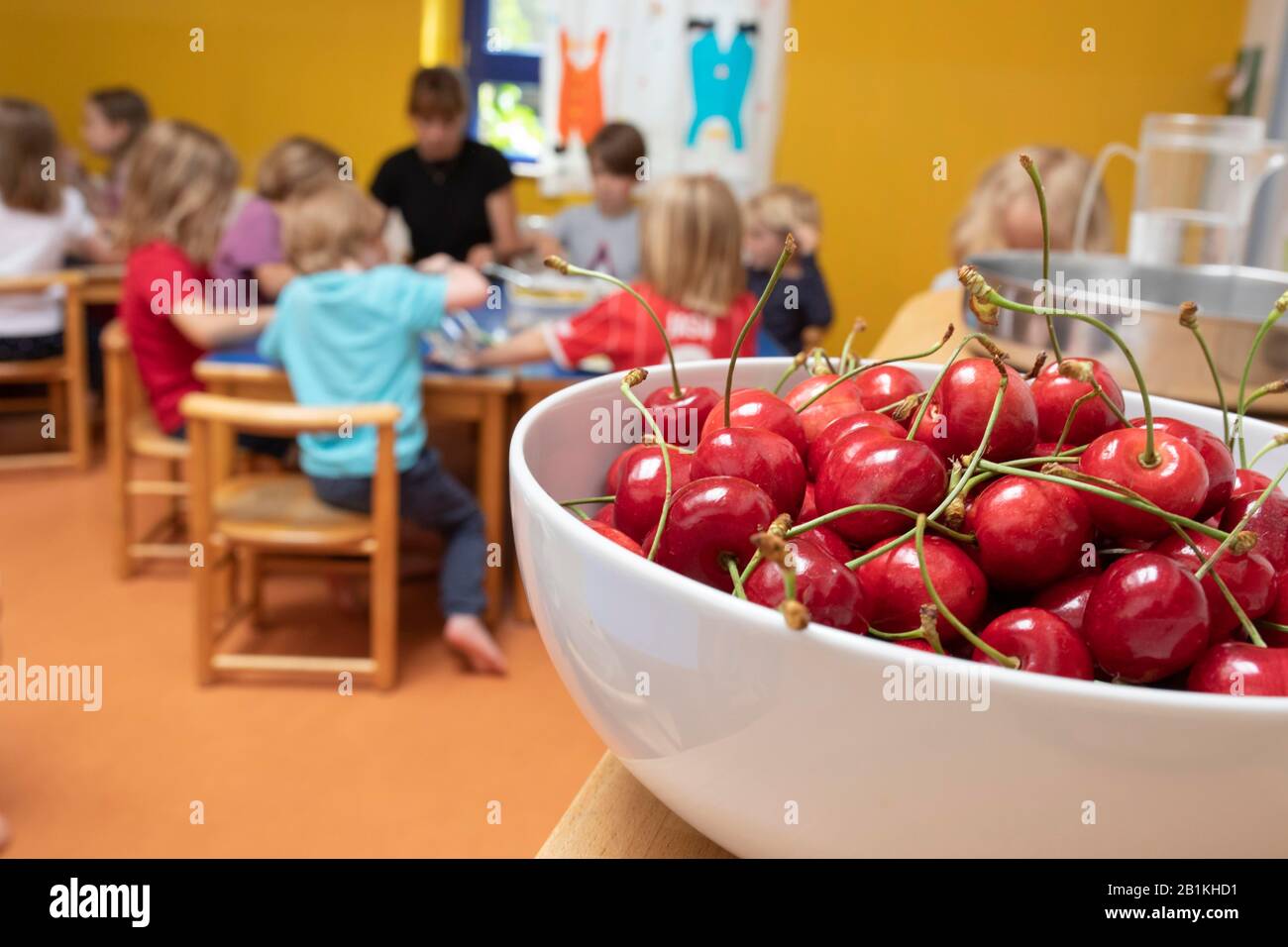 A bowl of cherries stands in the dining room in the kindergarten and children sit at the table to eat, Cologne, North Rhine-Westphalia, Germany Stock Photo