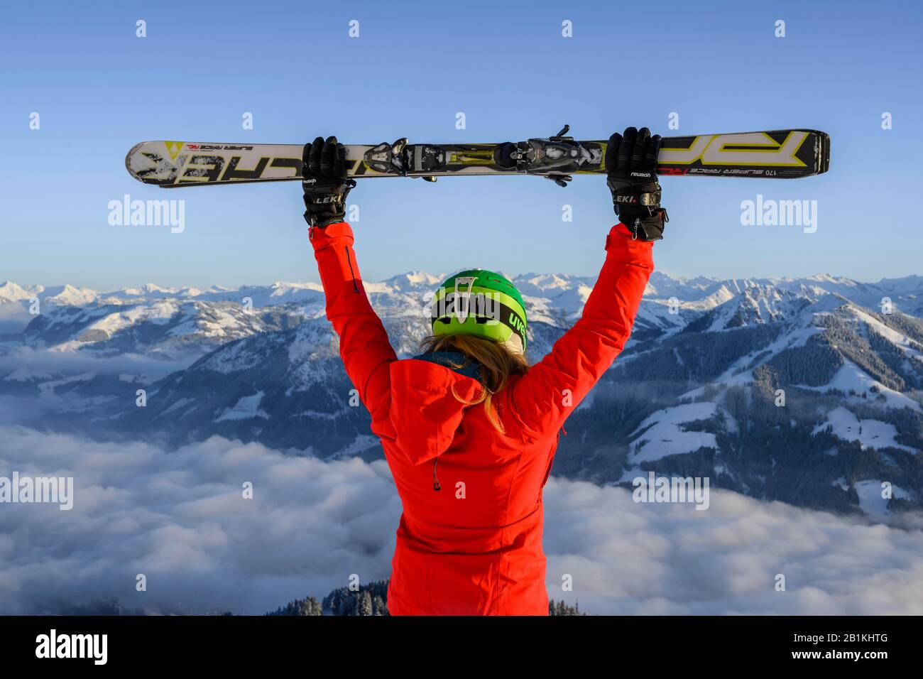 Skier with ski helmet holds ski in the air, behind her mountain panirama, SkiWelt Wilder Kaiser, Brixen im Thale, Tyrol, Austria Stock Photo